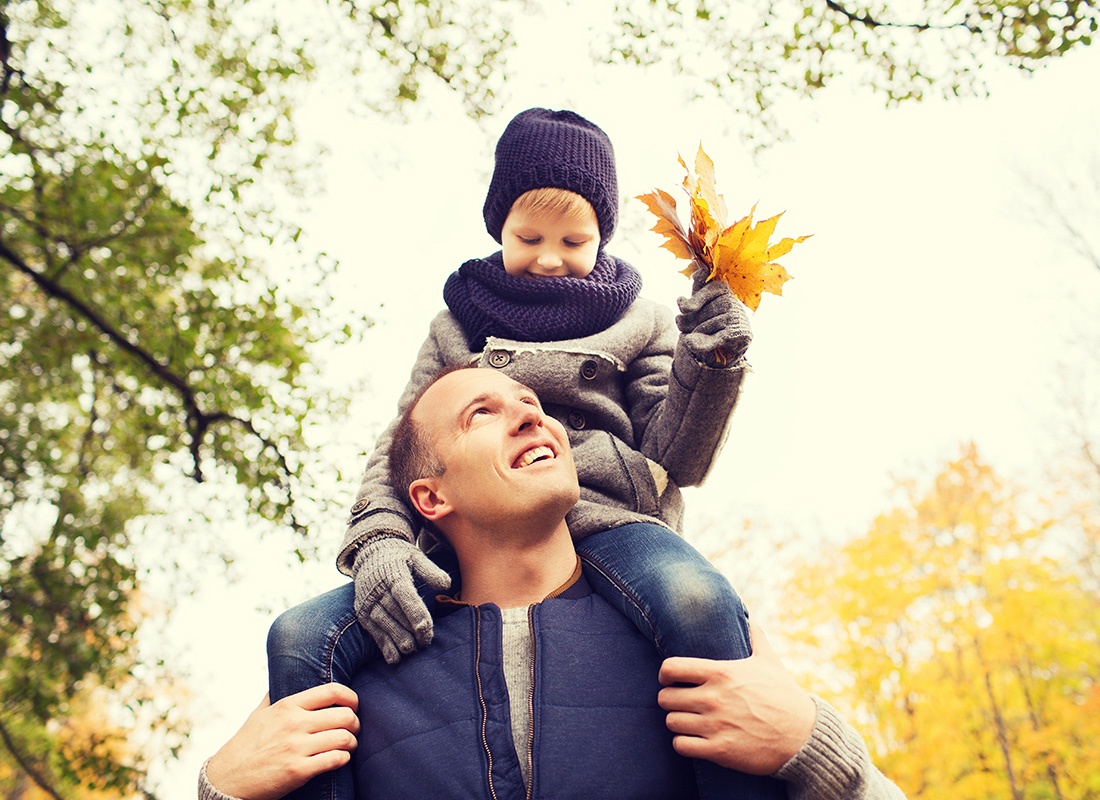 Contact - Portrait of a Smiling Father Holding his Son on his Shoulders as They Go for a Walk in the Park on a Chilly Fall Day