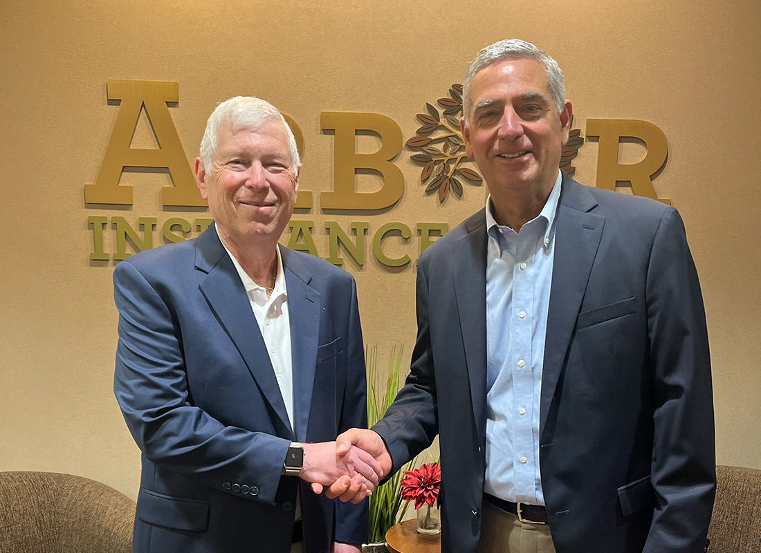 Block Insurance Agency - Block Insurance Agency Owner Shaking Hands with Arbor Insurance Group Owner in the Arbor Insurance Group Logo Behind Them in the Lobby